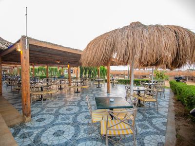 Offenes Restaurant mit Strohschirm und Holzmöbeln auf gepflastertem Boden im Freien.