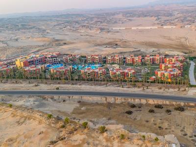 Große Hotelanlage mit bunten Gebäuden in einer Wüstenlandschaft, umgeben von Sand und Bergen.