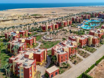 Große Hotelanlage mit mehreren roten Gebäuden und großen Swimmingpools in einer Wüstenlandschaft am Meer.