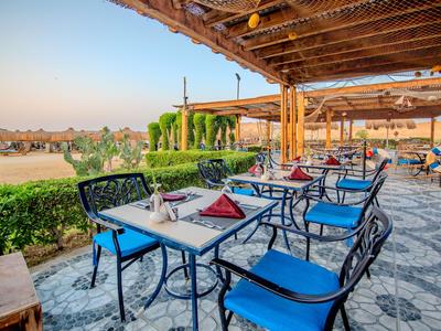 Offene Terrasse eines Hotels mit blau gepolsterten Stühlen und Blick auf einen Garten bei Sonnenuntergang.