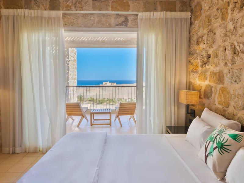 Dormitorio con pared de piedra y vista a la terraza y el mar bajo cielo despejado.
