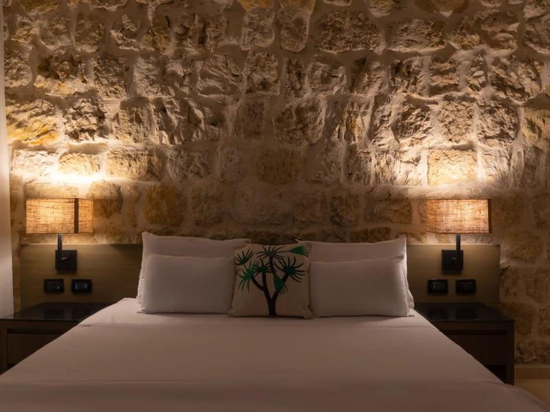 Habitación acogedora con pared de piedra, grandes almohadas y luz cálida.