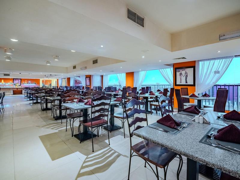 Restaurante luminoso con muchas mesas puestas y grandes ventanales con cortinas.