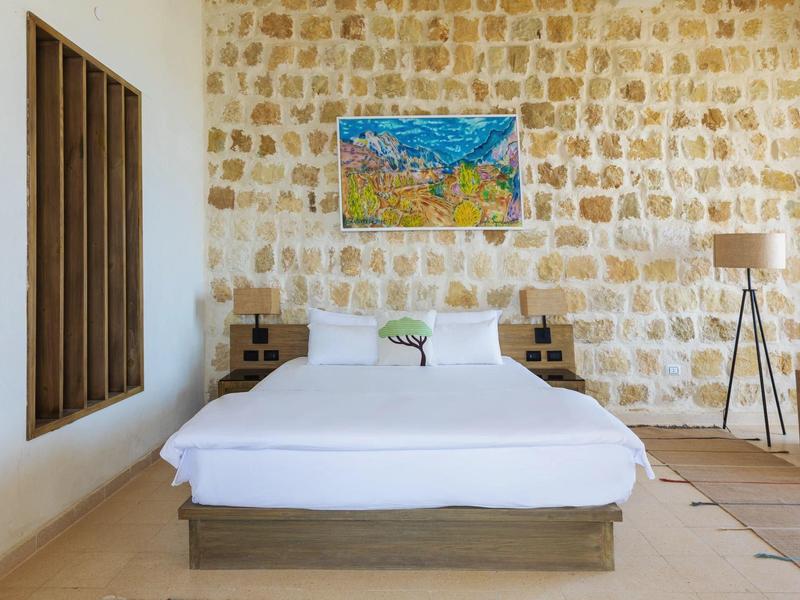 Habitación de hotel luminosa con pared de piedra, cama doble y cuadro colorido sobre el cabecero.