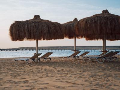 Sandstrand mit Strohdächern und Liegestühlen vor ruhigem Meer bei Sonnenuntergang.