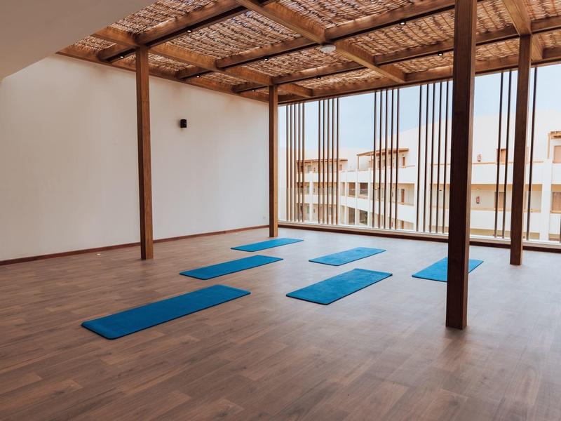 Espace de yoga ouvert avec tapis bleus et toit en bois avec vue sur des bâtiments.