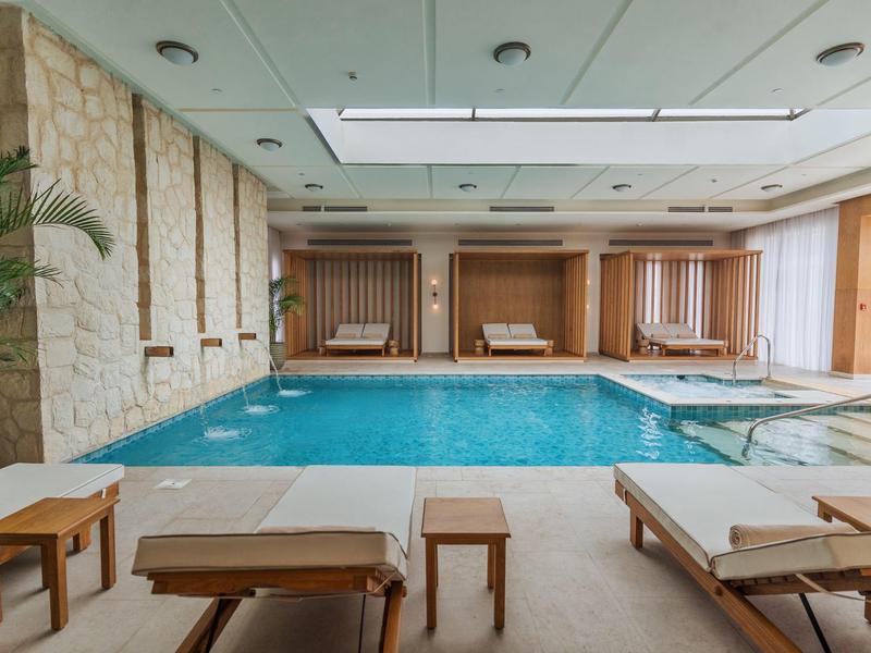 Piscine intérieure moderne avec chaises longues et panneaux en bois dans un hôtel.