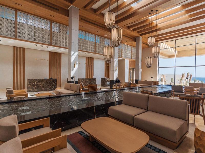 Salon d'hôtel moderne avec canapés confortables, poutres en bois et grandes fenêtres donnant sur la mer.