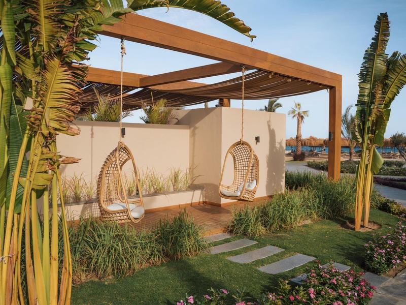 Coin salon confortable avec deux fauteuils suspendus et toit en bois dans un jardin.