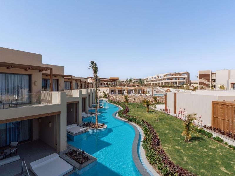Complexe hôtelier moderne avec une piscine serpentant entre les bâtiments sous un ciel dégagé.