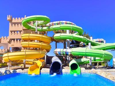 Colorful water slides lead into a pool in front of a castle-like structure under a clear sky.