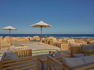 Open lounge area with wooden furniture and umbrellas on the beach under a clear blue sky.