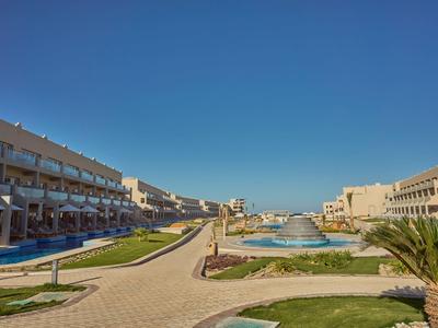 Complesso alberghiero moderno con vari edifici, piscine e giardini curati sotto un cielo limpido.
