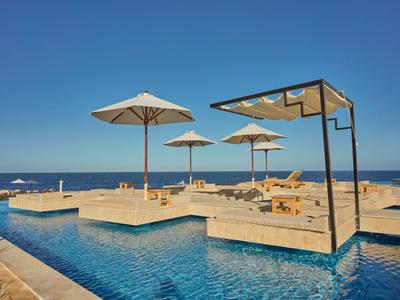 Modern pool area with sun loungers, umbrellas, and a sea view under clear skies.