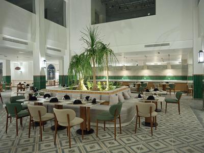 Bright hotel restaurant with high ceilings, plants, and elegant seating areas.