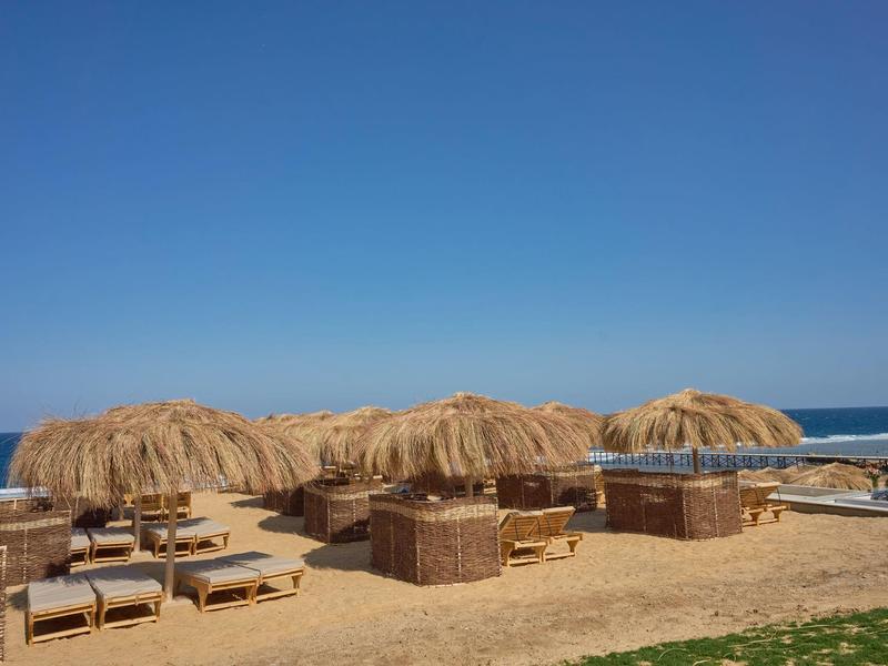 Beach with sand, sun loungers, and straw parasols under clear blue sky.
