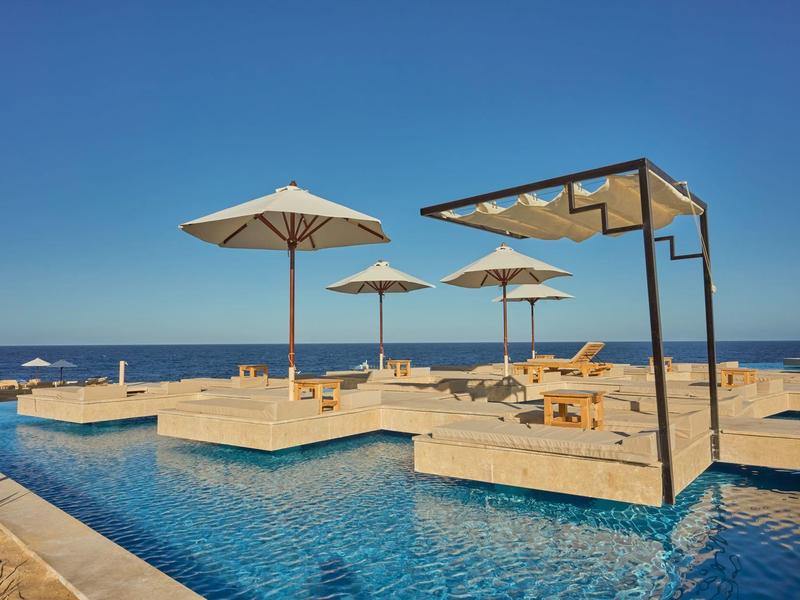 Modern pool area with white umbrellas and loungers by blue sky and sea