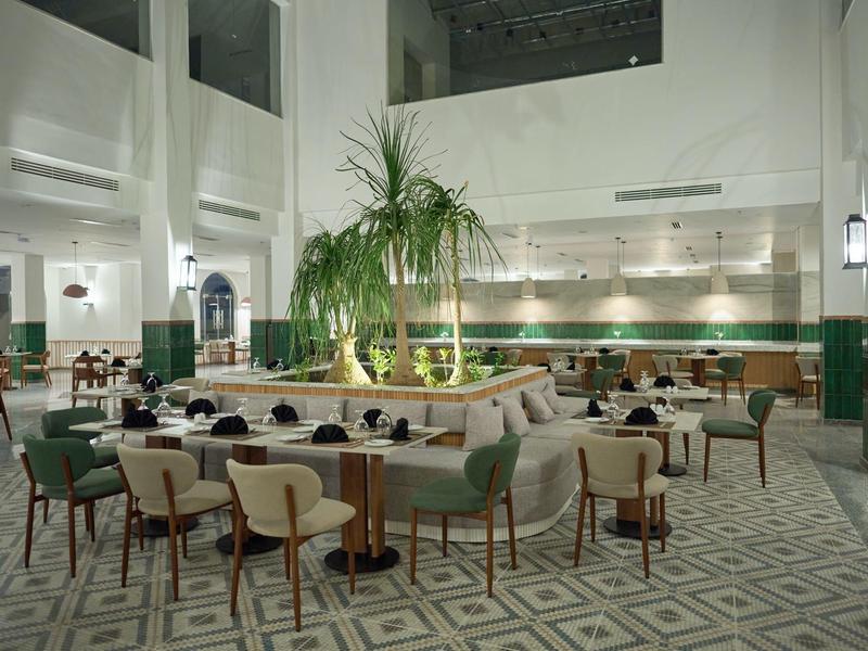 Interior of a modern hotel with green chairs, armchairs, and plants in a bright setting.