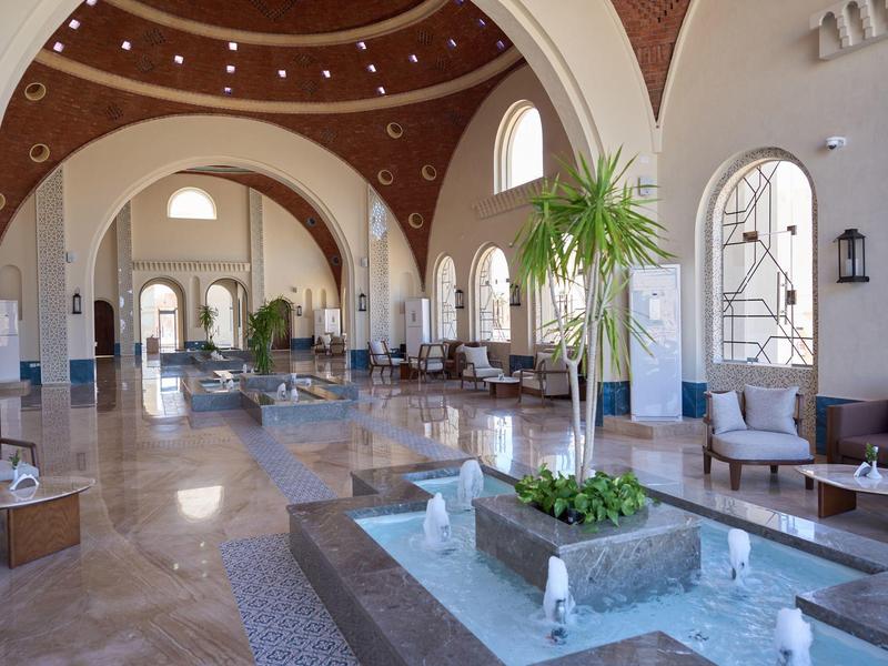 Bright hotel lobby with high arches, comfortable seating areas, and decorative fountain.