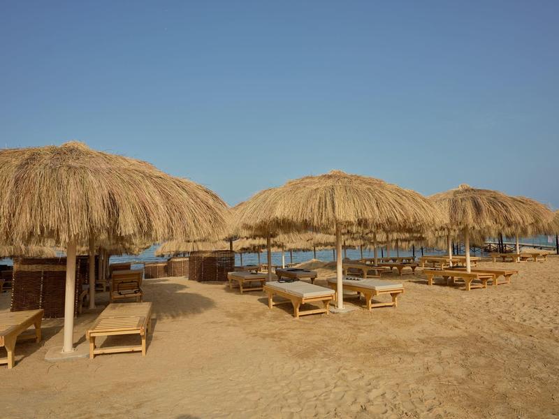 Beach with straw umbrella sunshades and lounge chairs under clear sky.