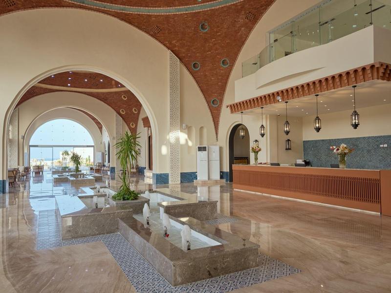 Bright hotel lobby with high vaulted ceilings, seating areas, and sea view.