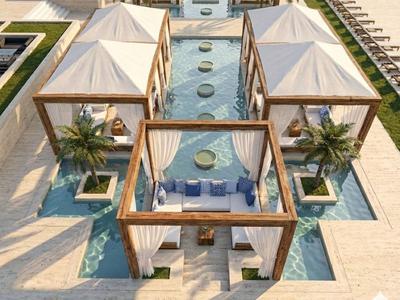 Cabanes de piscine luxueuses avec rideaux blancs et sièges confortables dans un complexe hôtelier.