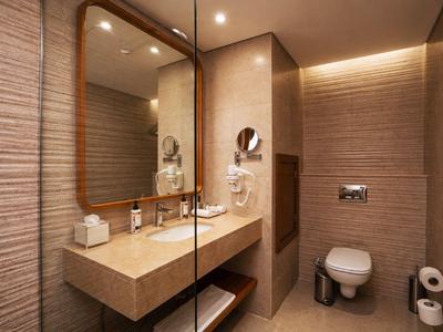 Bagno d'hotel moderno con grande specchio, lavabo e WC con illuminazione calda.