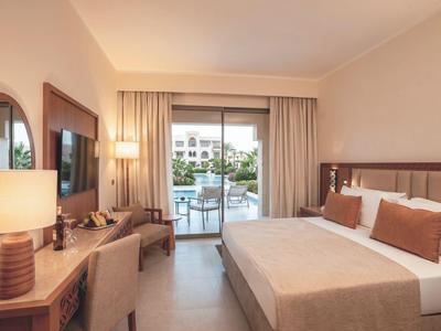 Camera d'albergo moderna con letto matrimoniale, TV, scrivania e terrazza con vista piscina.