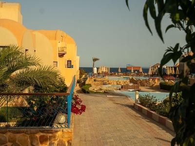 Sentiero lungo un hotel con piscina, palme e edifici gialli al tramonto.