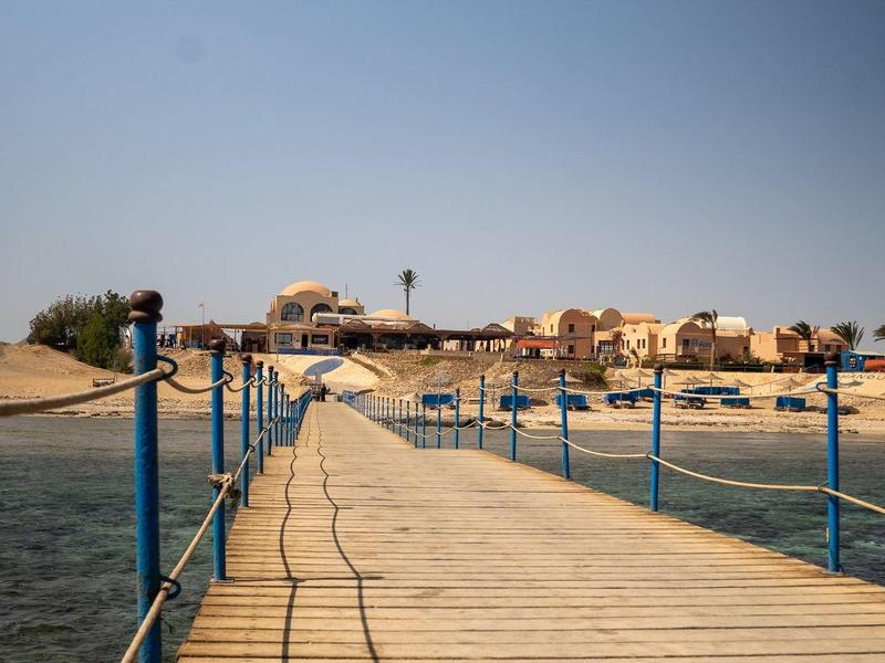 Une longue jetée en bois avec des rampes bleues mène à une station balnéaire sous un ciel dégagé.