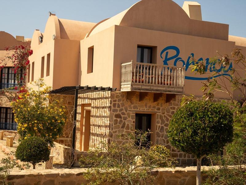 Bâtiment d'hôtel aux murs couleur sable avec des arbres devant sous un ciel clair.