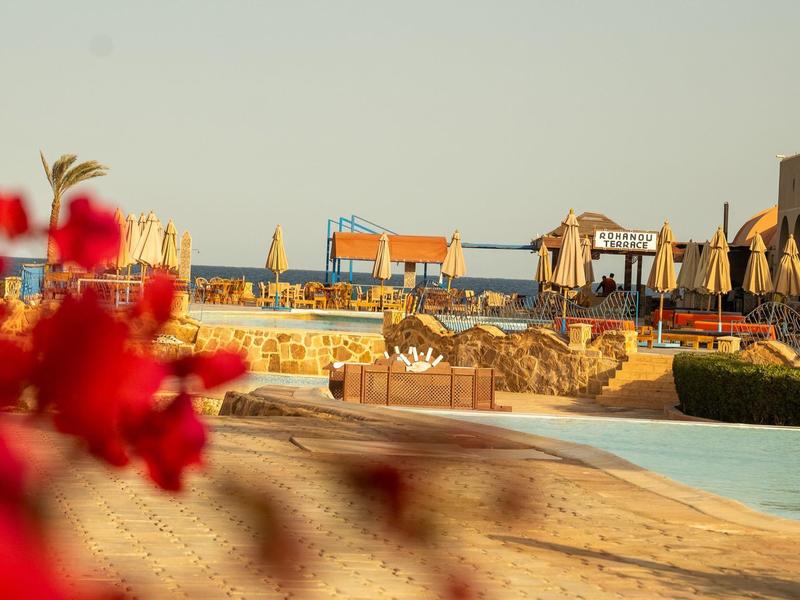 Plage avec transats et parasols devant un hôtel sous un ciel clair.