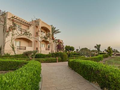 Sentiero conduce a un hotel su più piani con architettura mediterranea e giardino curato.