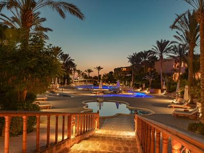Complesso alberghiero serale con piscina illuminata e palme sotto un cielo limpido.