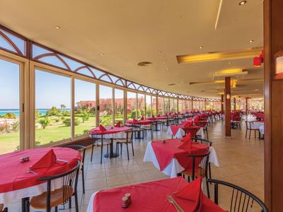 Ampia sala da pranzo con tavoli apparecchiati in rosso, vista sul mare attraverso grandi finestre.