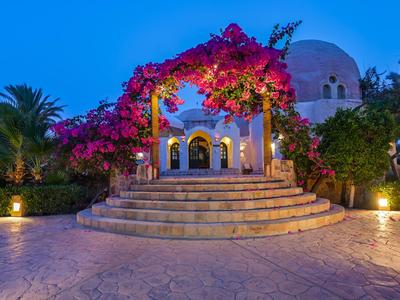 Padiglione illuminato con fiori e palme in un giardino tropicale al crepuscolo.