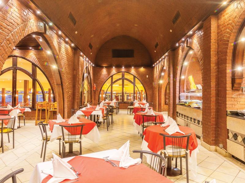 Elegancka restauracja z czerwonymi obrusami, łukami z cegieł i ciepłym oświetleniem.