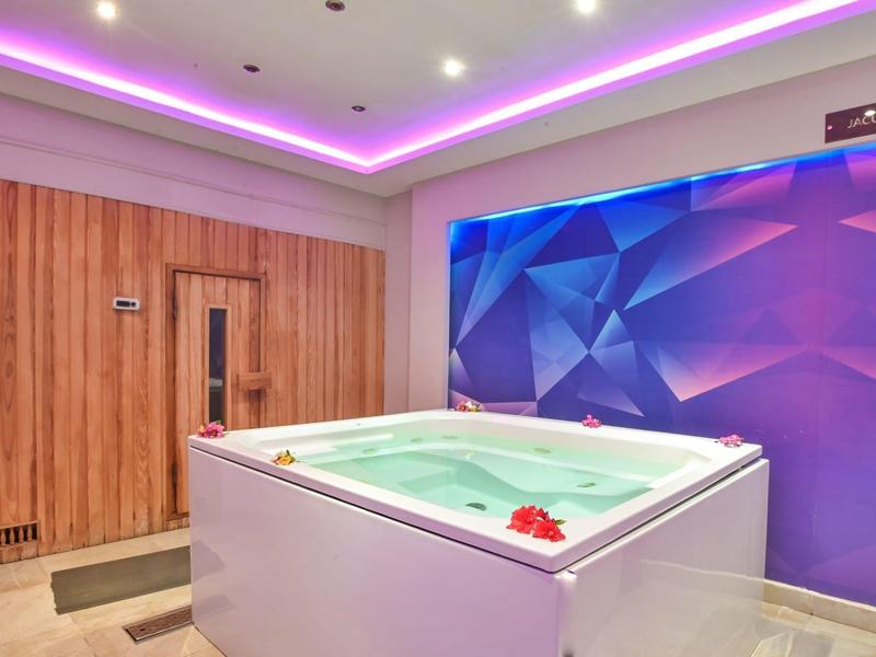 Nowoczesne jacuzzi z drewnianą sauną w relaksującym hotelowym otoczeniu z fioletowym oświetleniem.