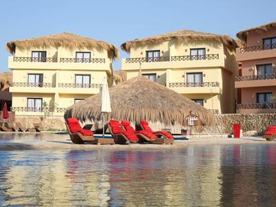 Hotel con bungalow con tetto di paglia e sdraio vicino alla piscina sotto un cielo blu
