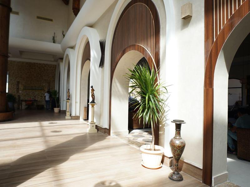 Couloir d'hôtel élégant et lumineux avec des chaises en bois et des plantes décoratives.