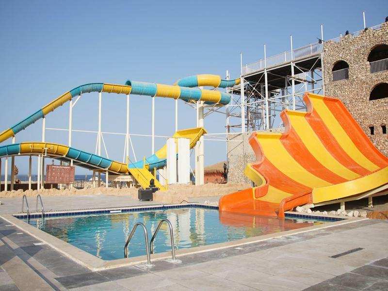Zone de toboggans aquatiques colorés à côté d'une piscine et d'une attraction château sous un ciel clair.