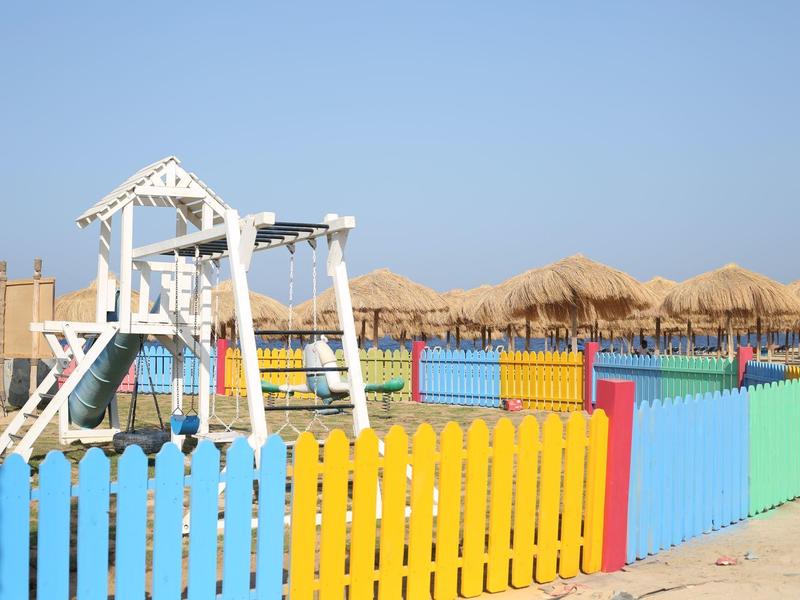 Clôture colorée autour d'une balançoire pour enfants sur la plage sous un ciel bleu.