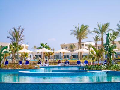 Großer Hotelpool mit blauer Mosaikfliese, Sonnenschirmen und Palmen unter klarem Himmel.