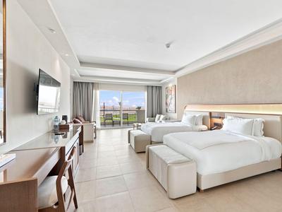 Modernes Hotelzimmer mit zwei großen Betten, Schreibtisch und Blick auf einen Balkon.