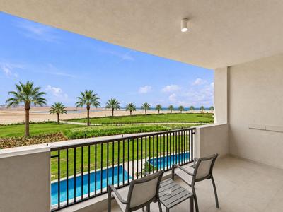 Balkon mit Stühlen bietet Blick auf Pool, Palmen und offene Landschaft bei blauem Himmel.