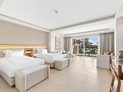 Modernes Hotelzimmer mit zwei Betten, großem Fenster und Blick auf Garten und Pool.