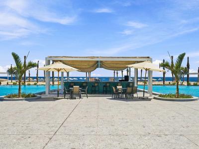 Ein Hotelpool mit schattigem Pavillon und Palmen vor klarem blauem Himmel.