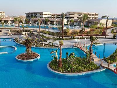 Große blaue Hotelpoolanlage mit Insellandschaften und Brücken vor Gebäuden im Urlaubsort.
