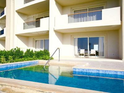 Moderne Hotelunterkunft mit Balkon und privatem Pool, umgeben von weißer Fassade und grünem Bewuchs.