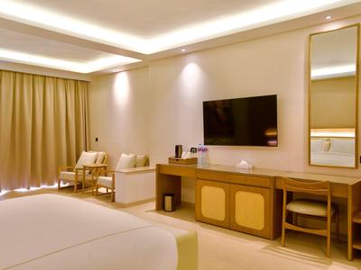 Modernes Hotelzimmer mit Bett, Fernseher, Vorhängen und Sitzbereich in warmem Licht.